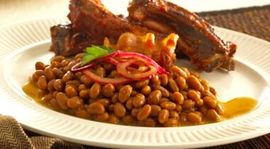 white plate with serving of baked beans garnished with onions and pork ribs