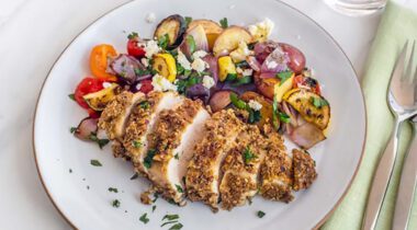 breaded sliced chicken breast on a white plate with cooked vegetables