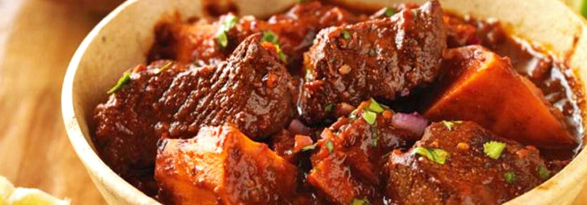 bowl of beef stew with big chunks of beef, sweet potato and spices