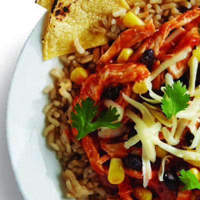 can of campbell's tomato soup beside a white bowl of cooked rice, chicken, black beans, corn, cheese, avocado