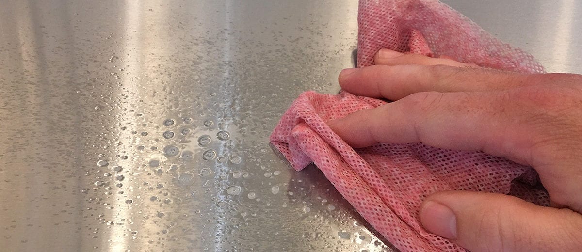 hand with red wiper cleaning metal surface