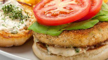 crab cake on a bun with lettuce, tomato, white sauce, herb sprinkled