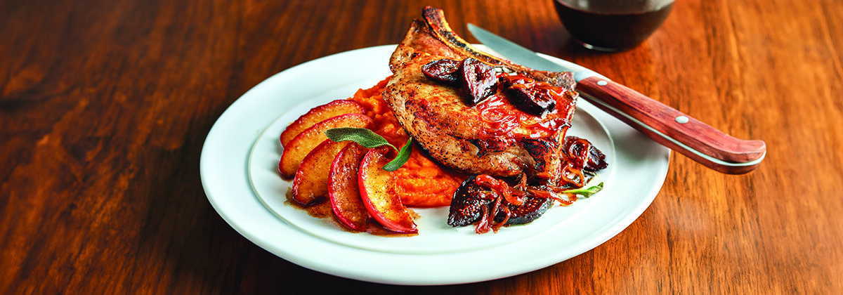 A white dinner plate, with a pork loin on top butternut squash, apple slices, fresh figs, and caramelized onions.