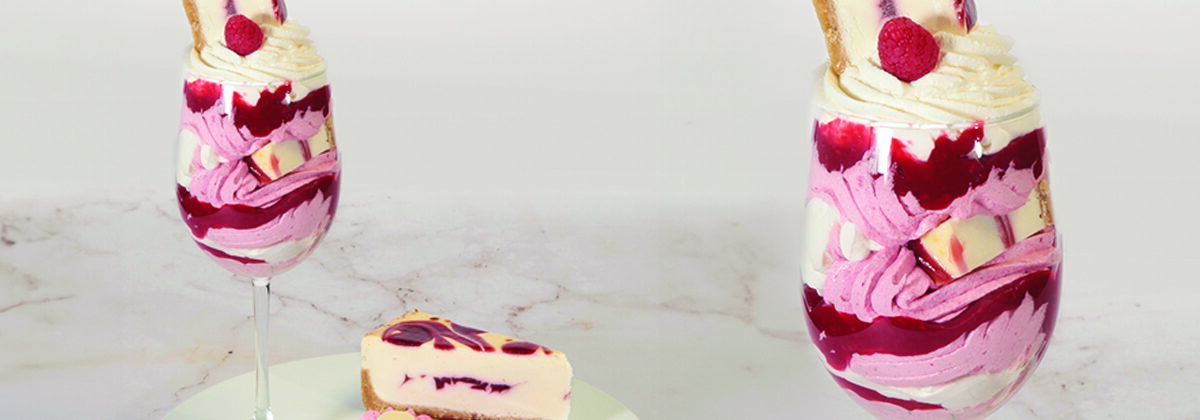 raspberry trifle dessert in wine glass next to plate with slice of raspberry cheesecake and another wine glass with close up of raspberry cheesecake trifle.