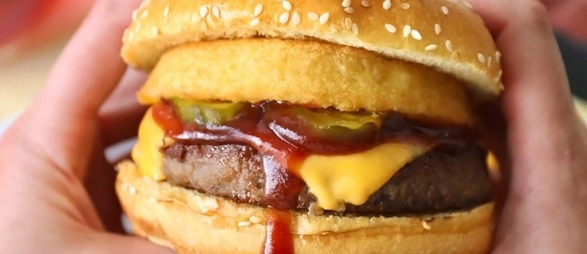 hands holding a cheeseburger with onion rings and pickles on it