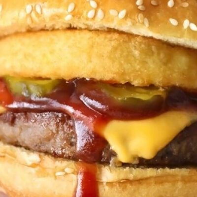 hands holding a cheeseburger with onion rings and pickles on it