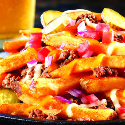 black plate loaded with french fries, hamburger, onions, tomatoes, shredded cheese, peppers ready to eat. ketchu and class of cold beer in background.