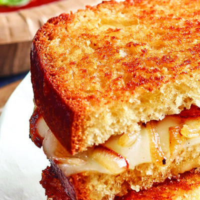 grilled cheese sandwich sliced, stacked on top of each other on plate with bowl of soup in background