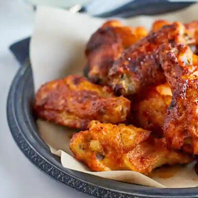 Tyson logo graphic image over white table with black plate of cooked chicken wings with sliced vegetables, dipping sauce.