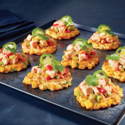 black plate of corn cake appetizers topped with turkey salad