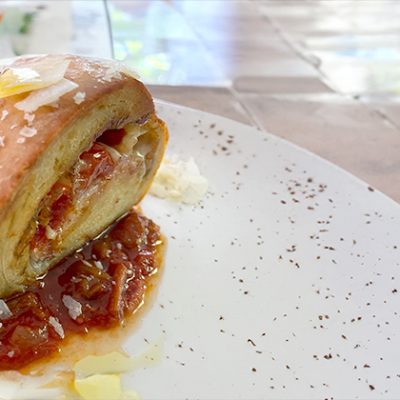 a speckled plate with a Pancetta Bread Roll in the middle on a bed of red sauce, sprinkles with Parmesan cheese.