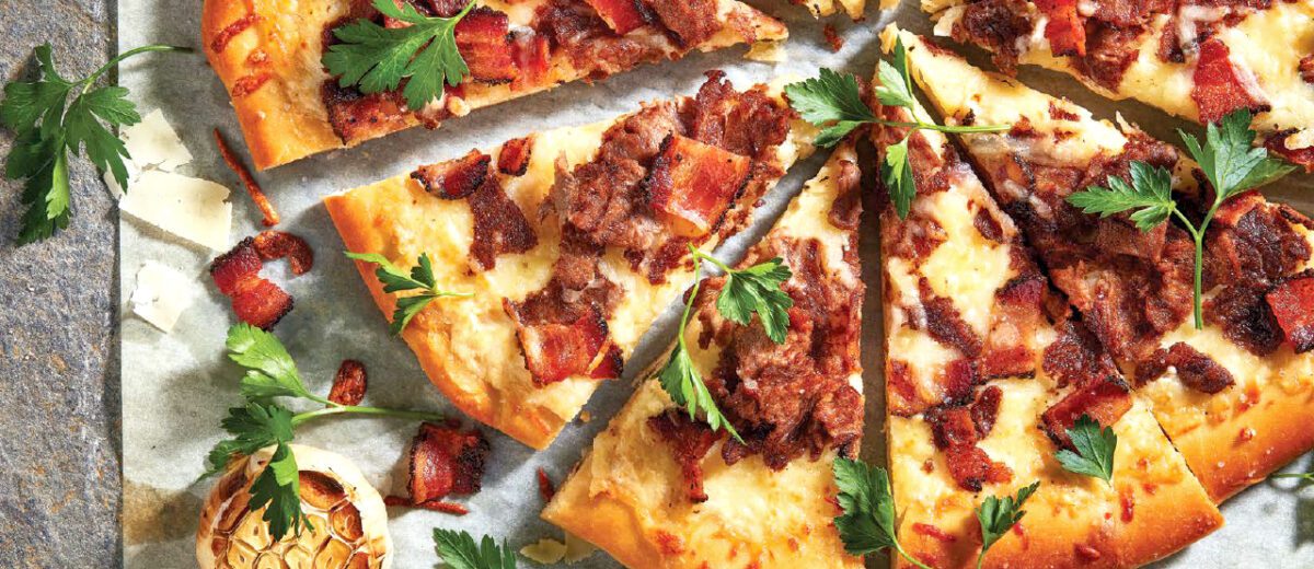 steak and bacon pizza, fresh parsley, slices of cheese, garlic head on granite stone