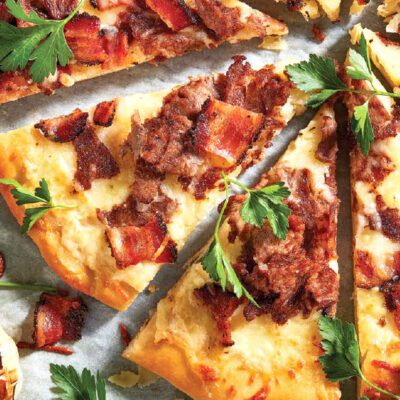 steak and bacon pizza, fresh parsley, slices of cheese, garlic head on granite stone