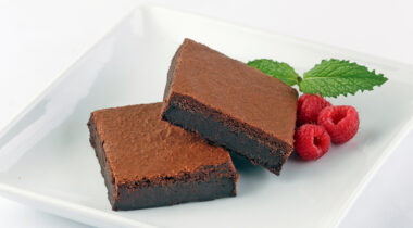 Deluxe fudge brownies on a white plate with three raspberries and a sprig of mint